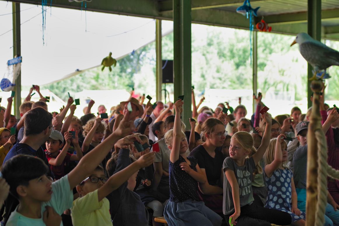 Gruppe von Kindern, die aufmerksam bei einer Veranstaltung im Freien sitzen.